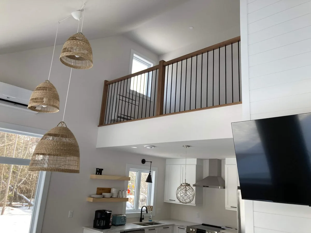 The great room looking up to the loft catwalk, with rattan pendant lights and the TV wall