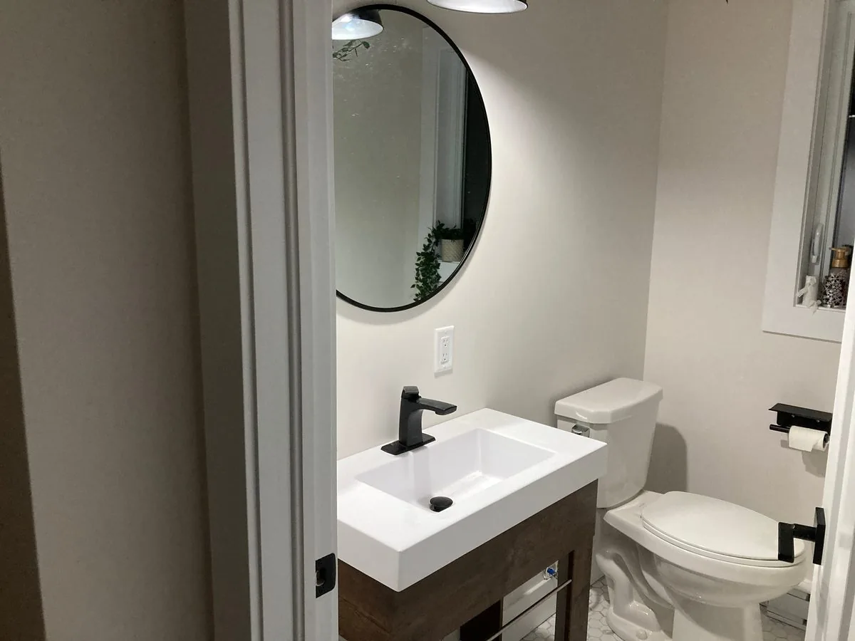 The upstairs half bath with a round mirror and black fixtures