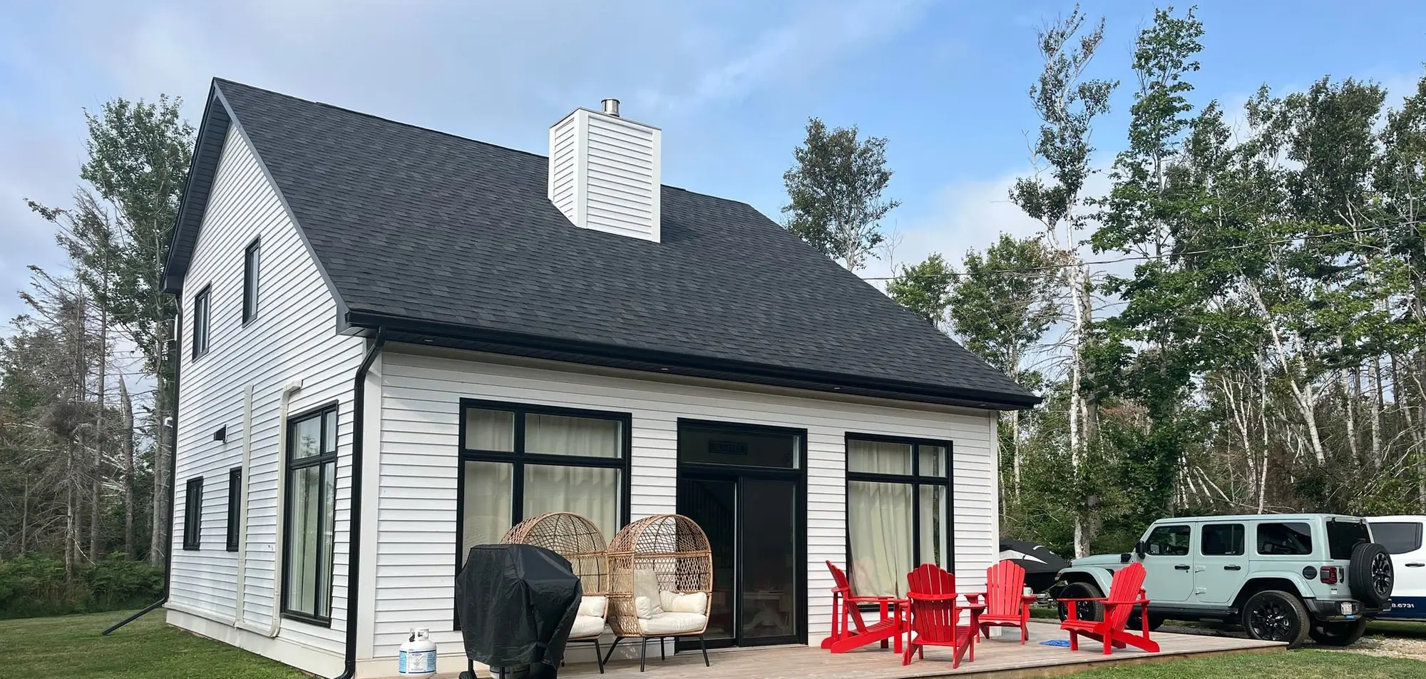 The front of Inner Beach Retreat in daylight, white siding with black window trim, red Adirondack chairs on the deck