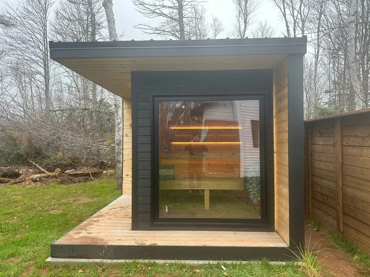 The sauna, a black and cedar cabin with a glass door, on its own deck