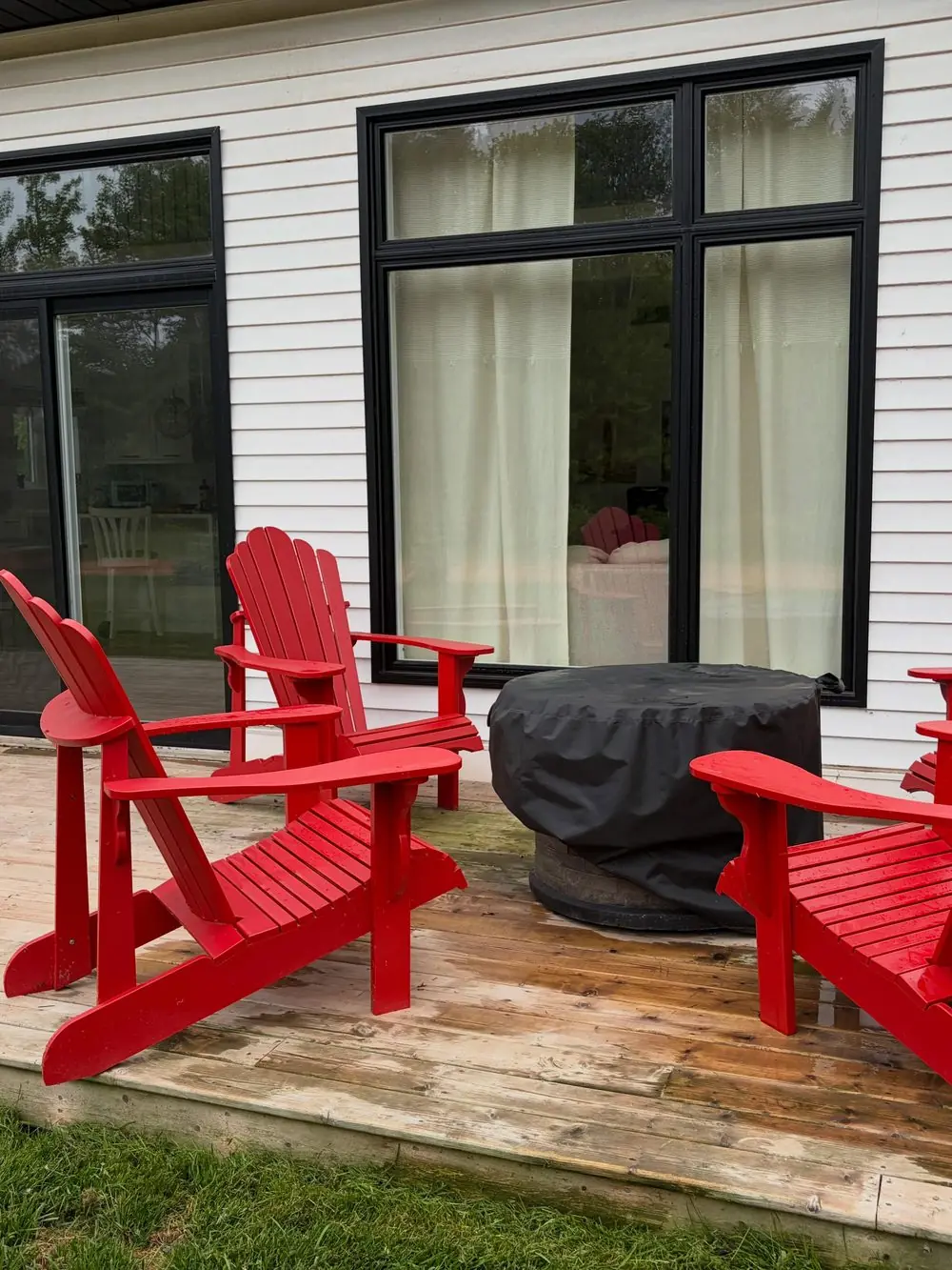Red Adirondack chairs around the covered propane fire table on the front deck