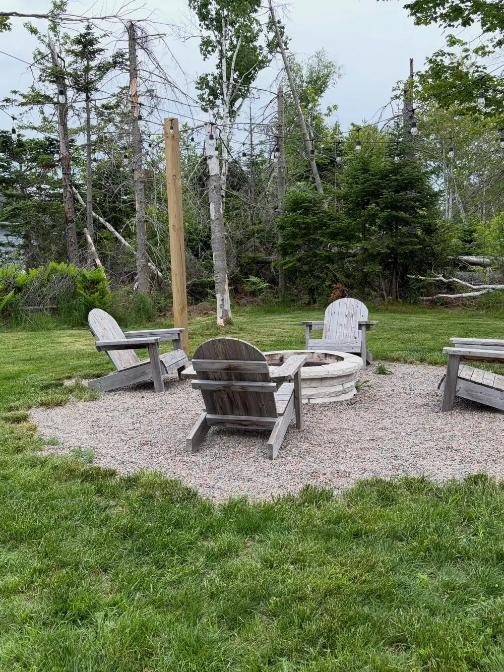 The fire pit circle on gravel with Adirondack chairs and birch and spruce behind